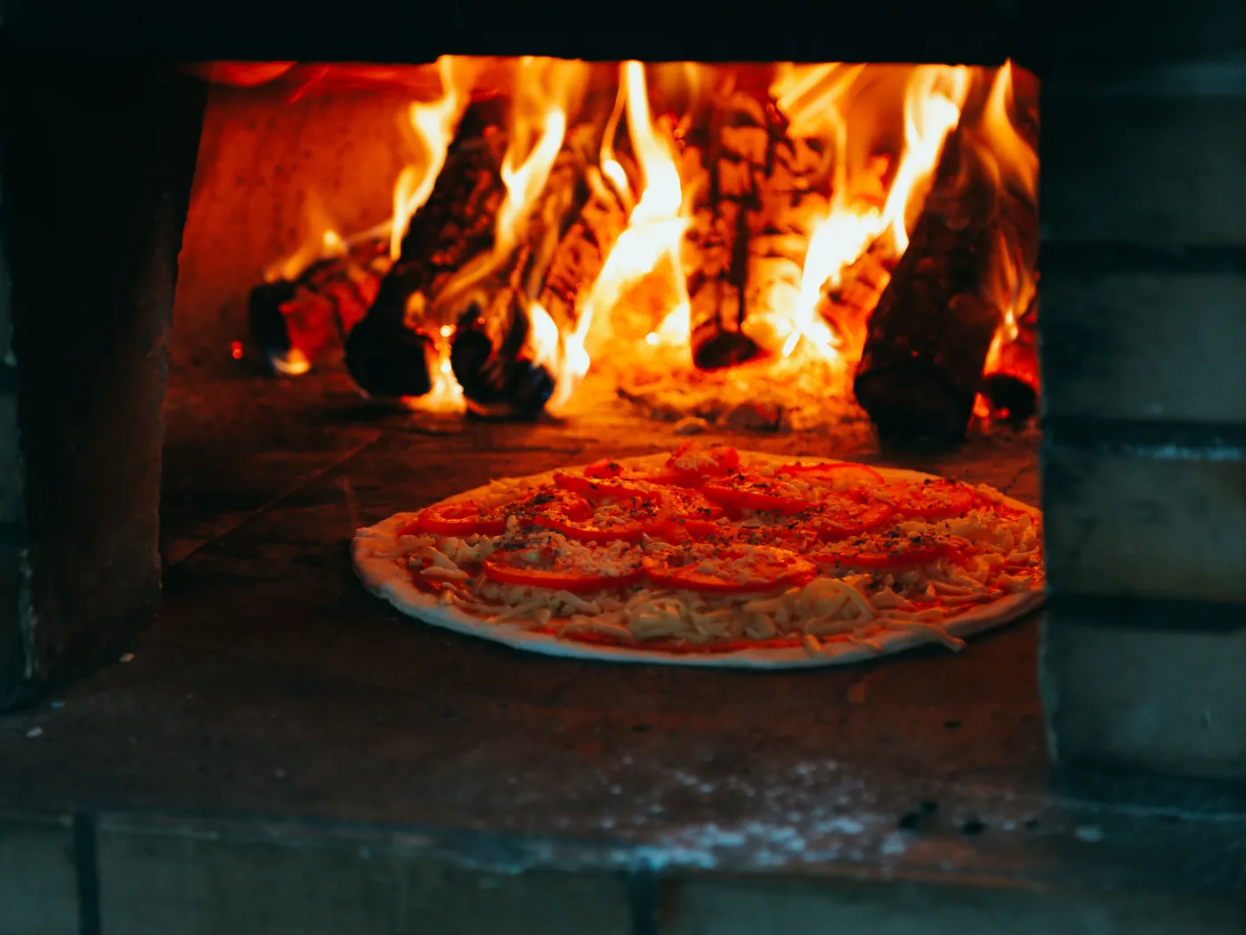 Rajčatová pizza na dně cihlové pece pod řvoucím dřevěným ohněm